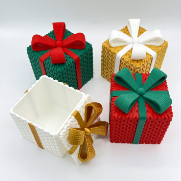 Set of four 3D printed gift boxes with a knitted texture. The collection includes red, green, gold, and white boxes with contrasting ribbons. The white box is open to show the interior storage space.