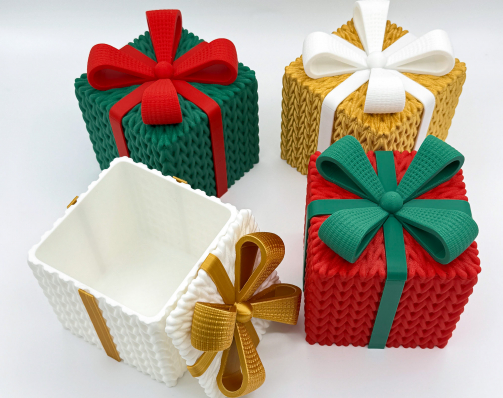 Set of four 3D printed gift boxes with a knitted texture. The collection includes red, green, gold, and white boxes with contrasting ribbons. The white box is open to show the interior storage space.