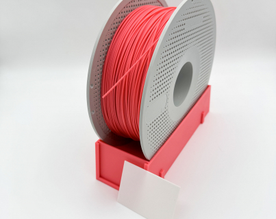 Pink 3D printing filament spool stand holding a grey Bambu Lab reusable spool, featuring a blank white label card in the foreground for filament identification printing settings.