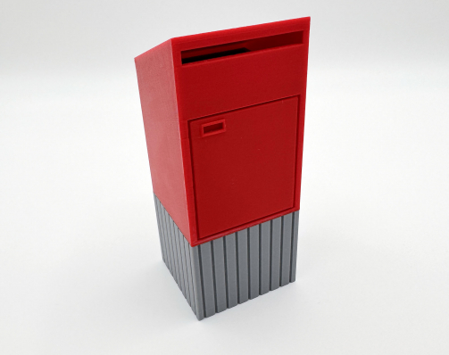 Red miniature mailbox desk organizer with grey base, used as a paper clip holder or stamp dispenser.