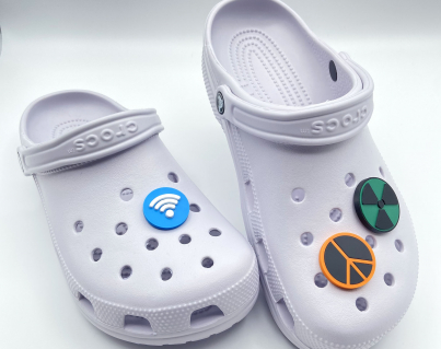 Two white clogs displaying 3D printed Wi-Fi, Peace, and Nuke symbols as charms.