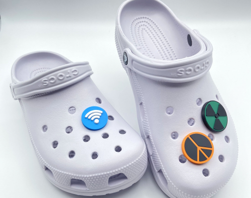 Two white clogs displaying 3D printed Wi-Fi, Peace, and Nuke symbols as charms.