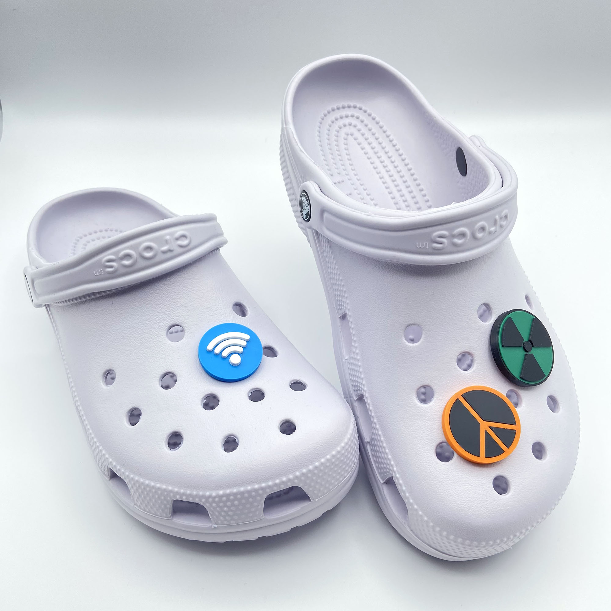 Two white clogs displaying 3D printed Wi-Fi, Peace, and Nuke symbols as charms.