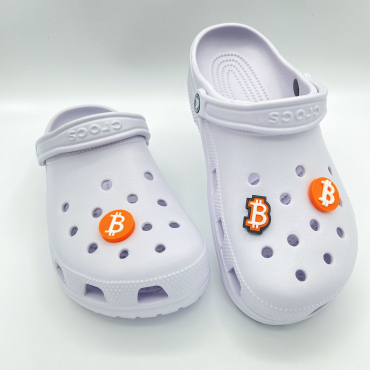 A pair of white clogs featuring a collection of three different 3D printed orange Bitcoin shoe charms.