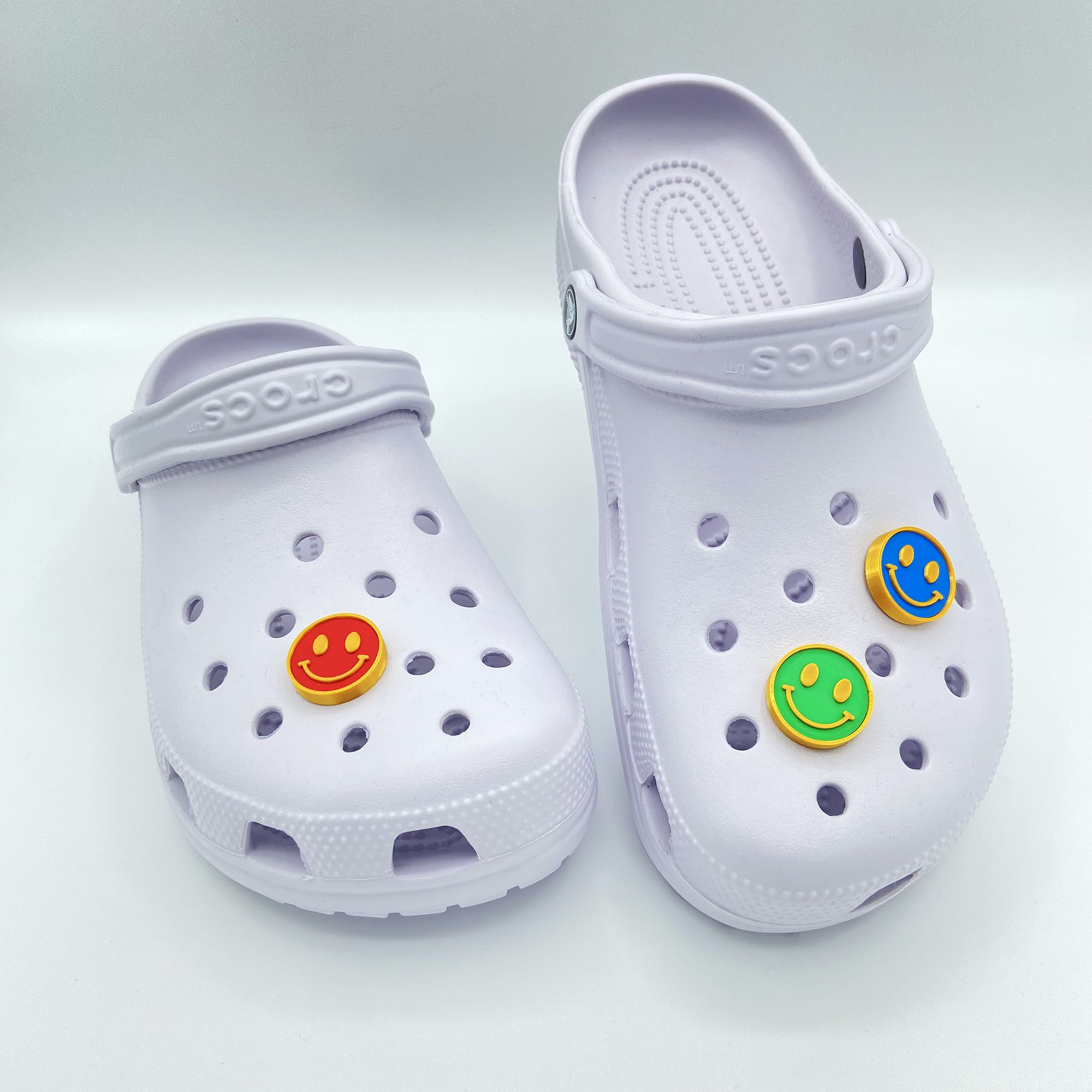 Red, green, and blue smiley face charms on white clogs.