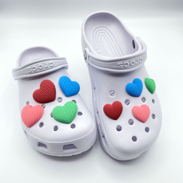 Small and large 3D printed heart charms in multiple colors on a pair of light purple Crocs.