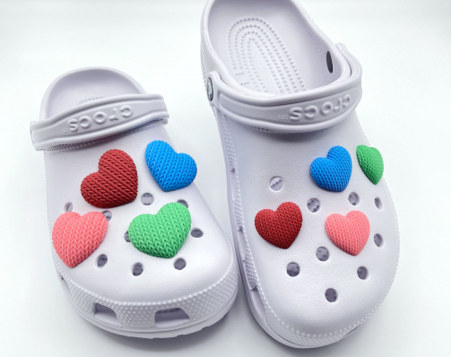 Small and large 3D printed heart charms in multiple colors on a pair of light purple Crocs.